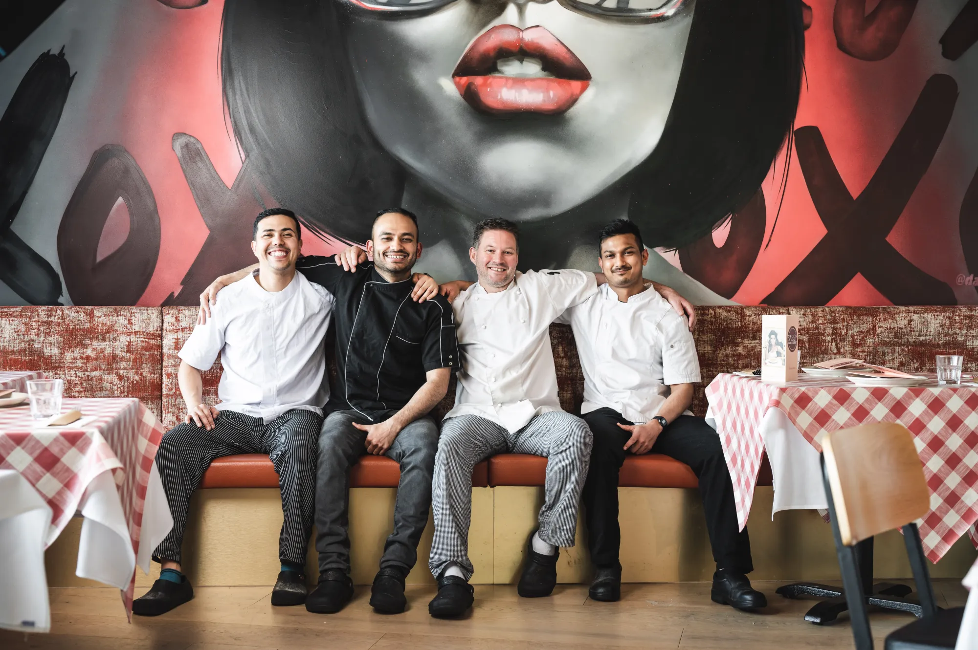 four italian restaurant chefs sat smiling with arms around each other