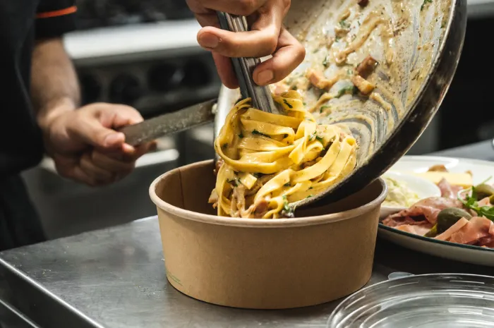 fettuccine pasta being twisted from a pan into a food box